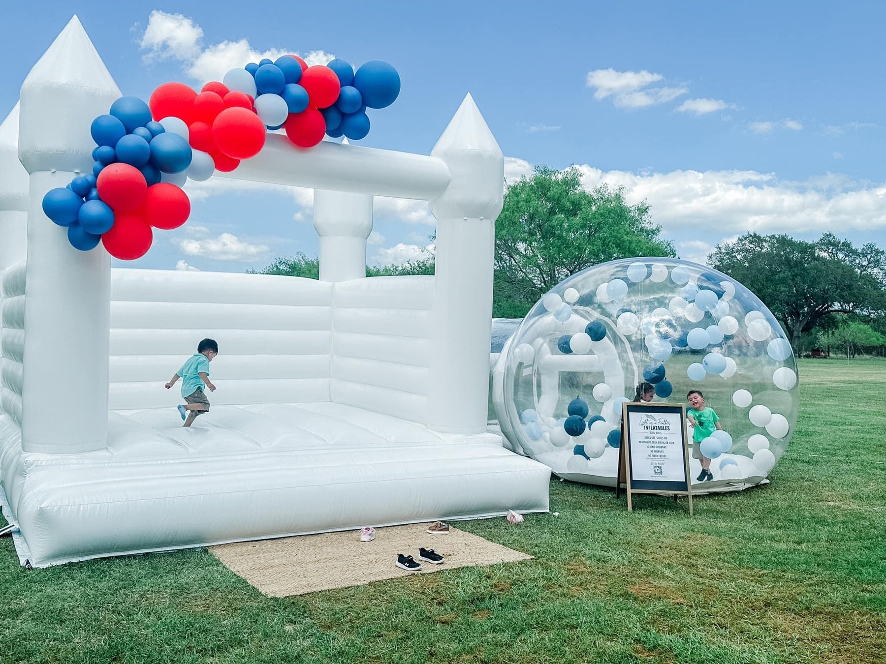 White bounce house and balloon-filled bubble tent at an outdoor celebration